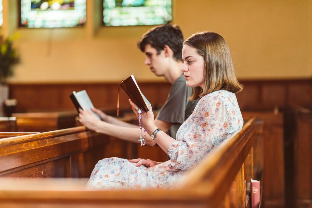 przygotowanie do bierzmowania Two young adults seated in a church pew, deeply engaged in prayer and reading.